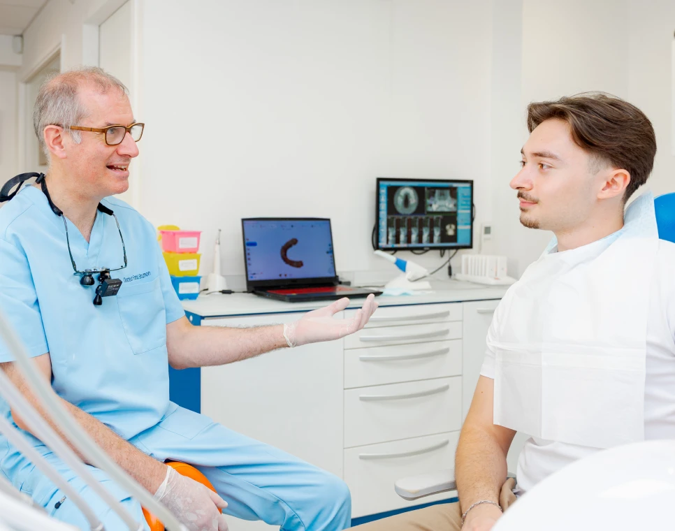 Dentiste échangeant avec un jeune patient au fauteuil, radiographie à l’écran